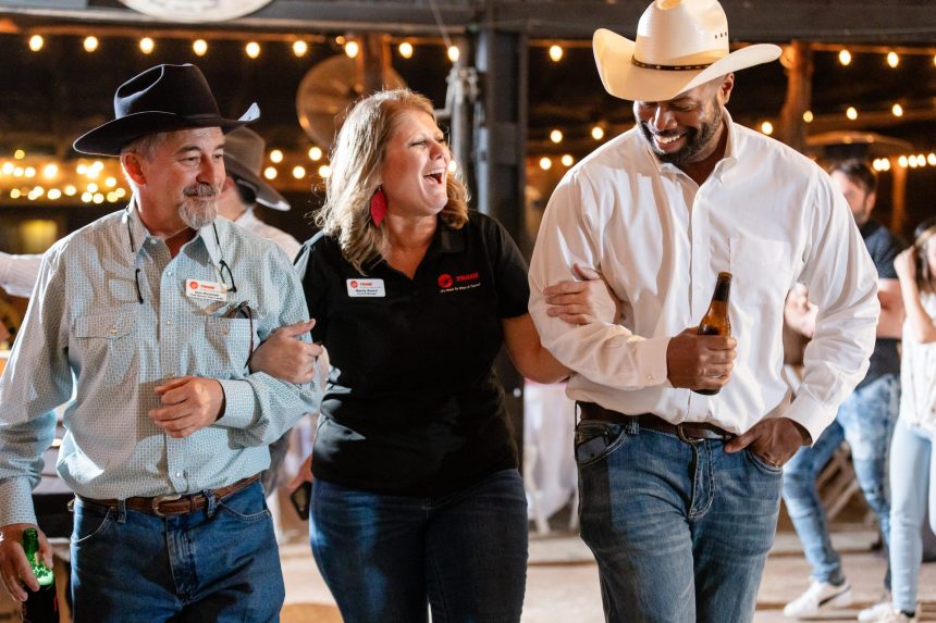 Three guests arm in arm and laughing on the dance floor of the Silver Spur Saloon under string lights